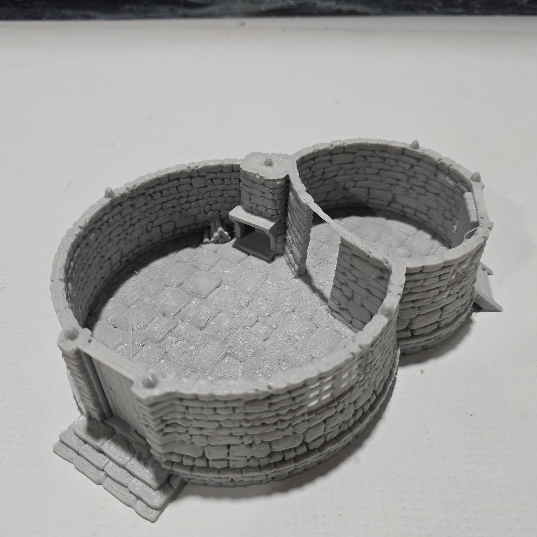 A highly detailed 3D-printed model of the Dragonspire Gamekeeper&#39;s Lodge, featuring two rooms, a fireplace with chimney, front and back doors, and a round roof design.